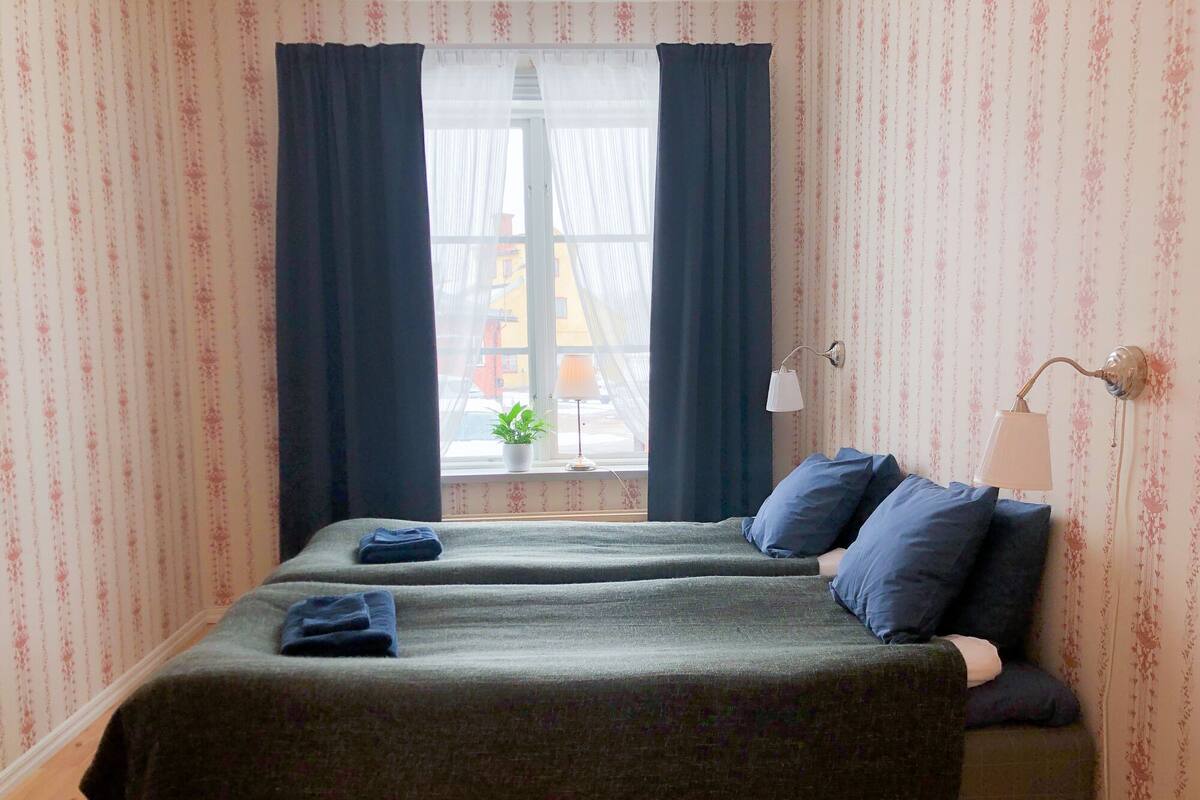 Une chambre avec deux lits, une fenêtre avec des rideaux, une lampe et une plante.