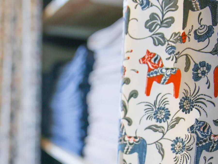 A fabric with a floral pattern, possibly a curtain or upholstery, hanging in a room with shelves in the background.