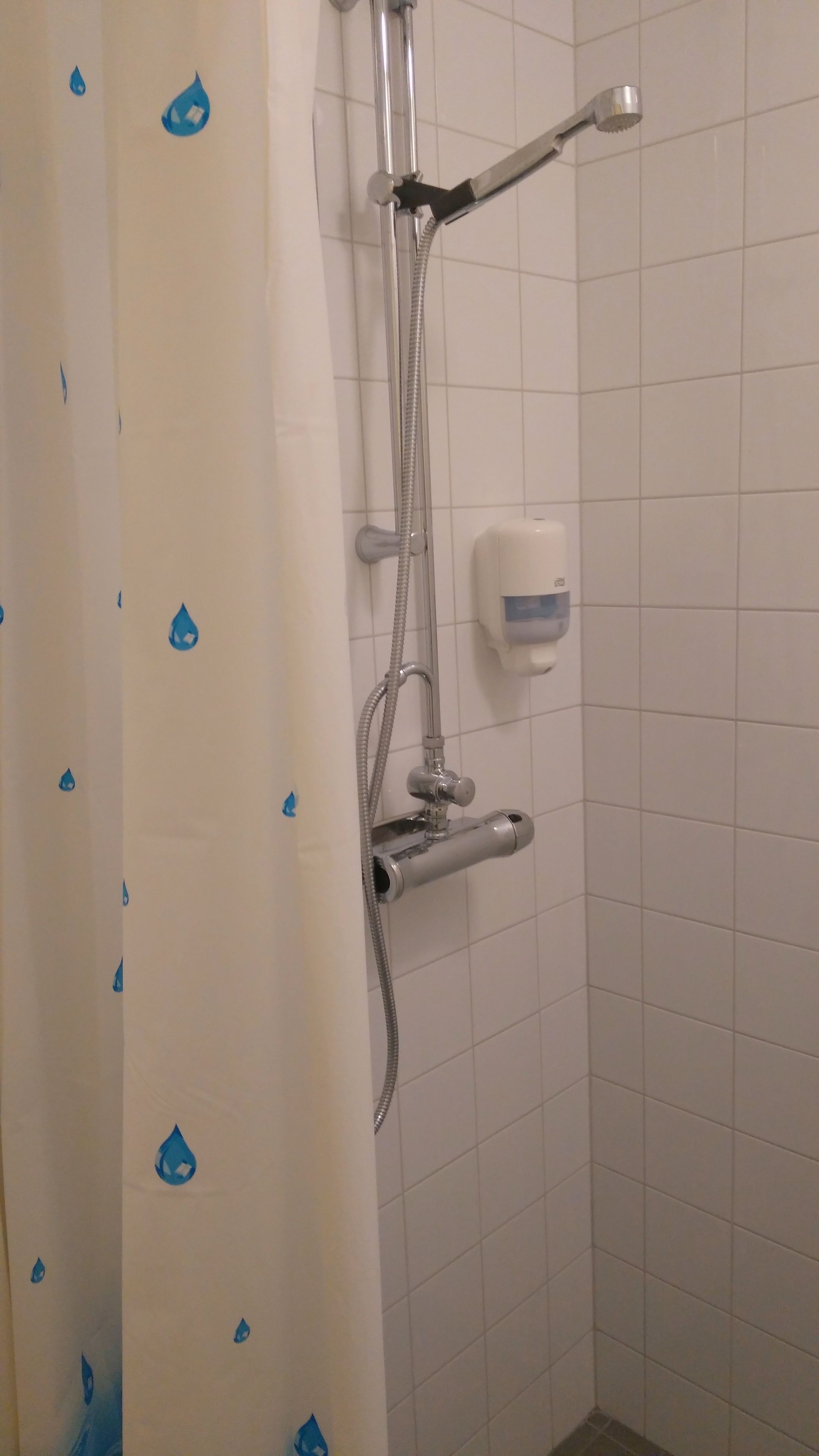Un área de ducha con ducha de mano, grifo de mano y dispensador de jabón en la pared.