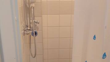 A small bathroom with white tiles, a shower with a handheld showerhead, and a blue shower curtain with water droplet patterns.