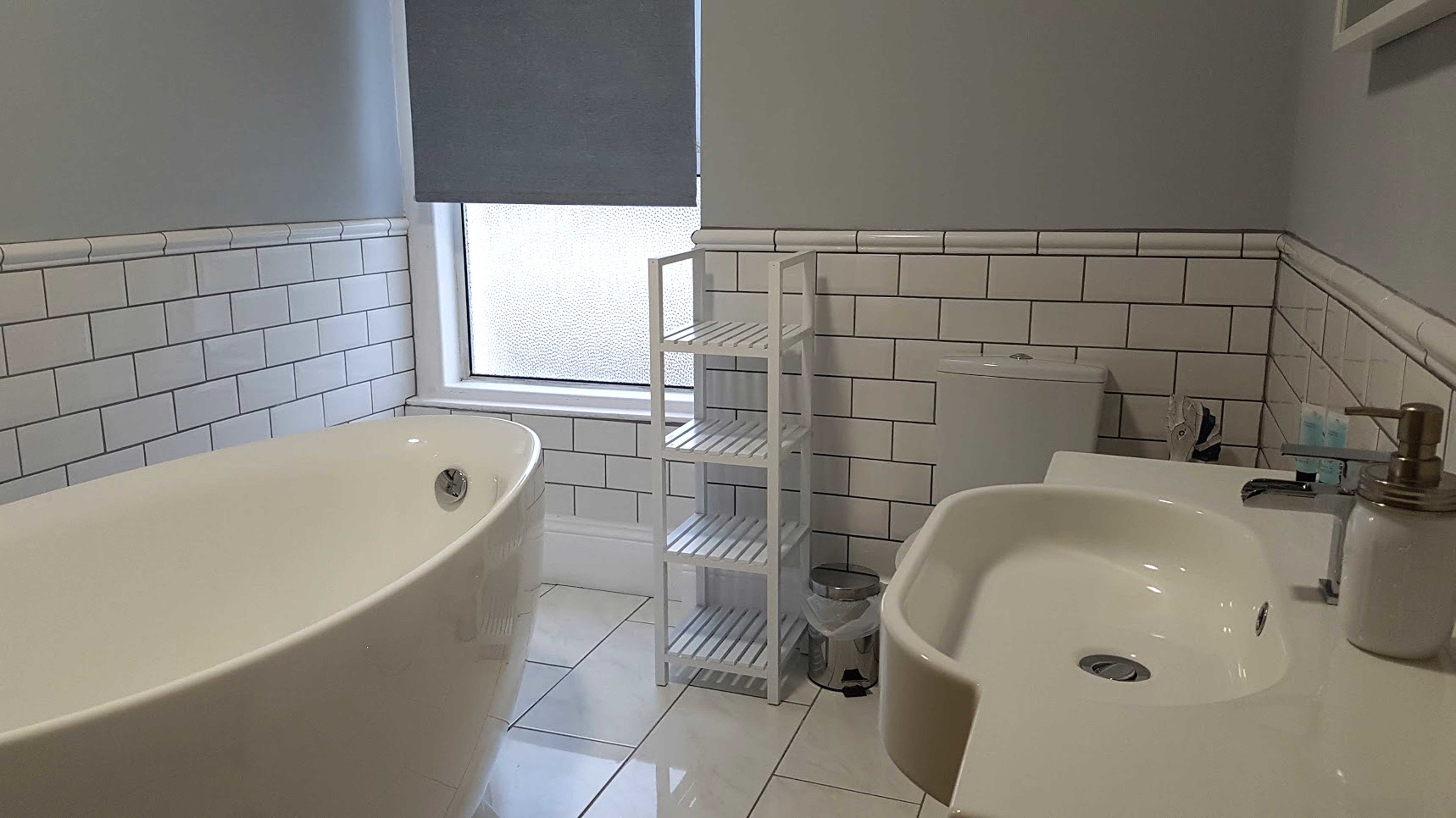 Un baño con bañera, lavabo e inodoro. Hay una ventana con vistas al exterior.
