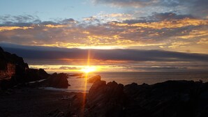 Ein Sonnenuntergang über einer felsigen Küste, die Sonne tief am Horizont und ein warmes Licht über die Szene werfend.