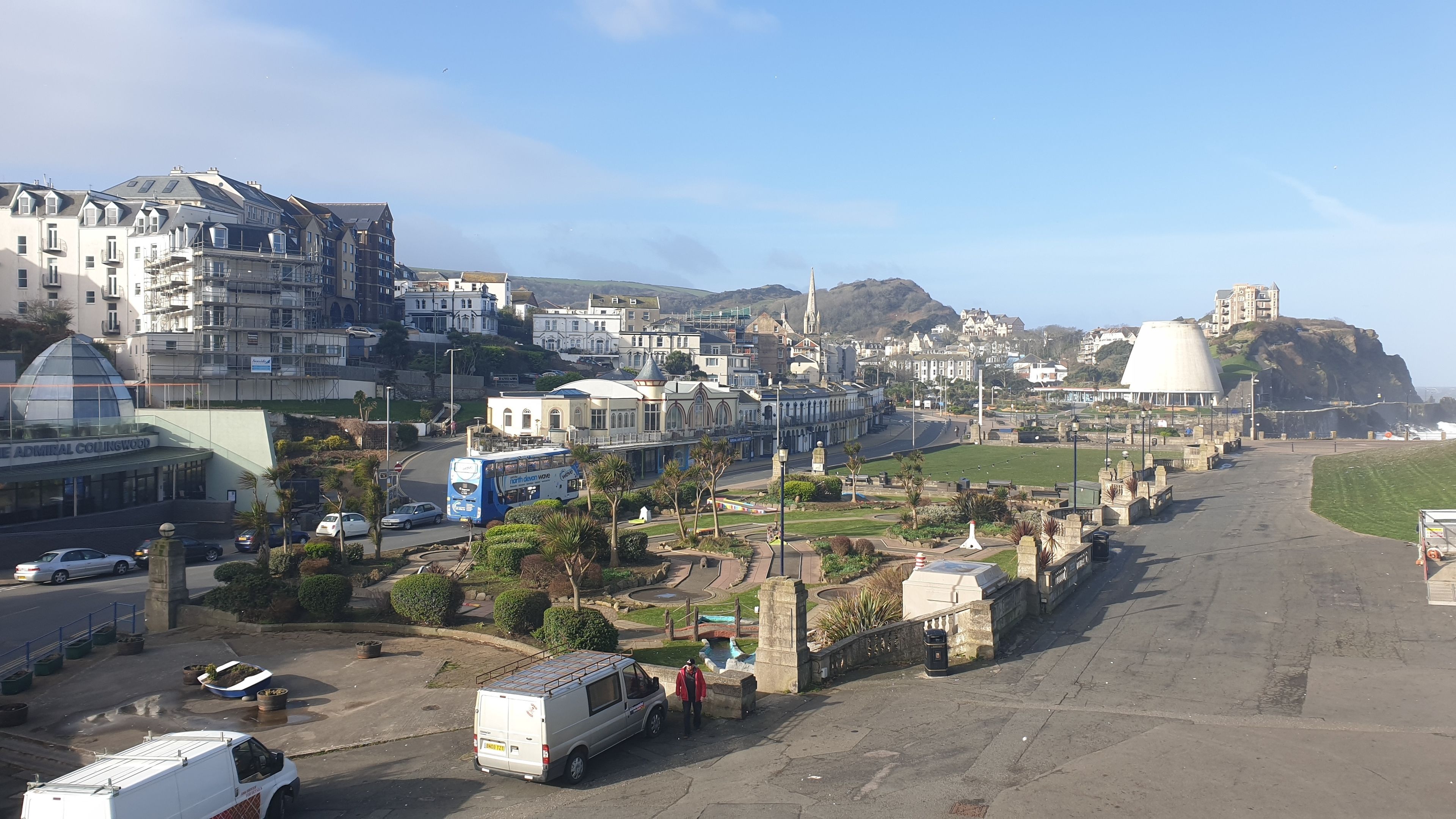 Un pueblo costero con una mezcla de edificios residenciales y comerciales, una estructura abovedada blanca destacada y una vista despejada del mar.