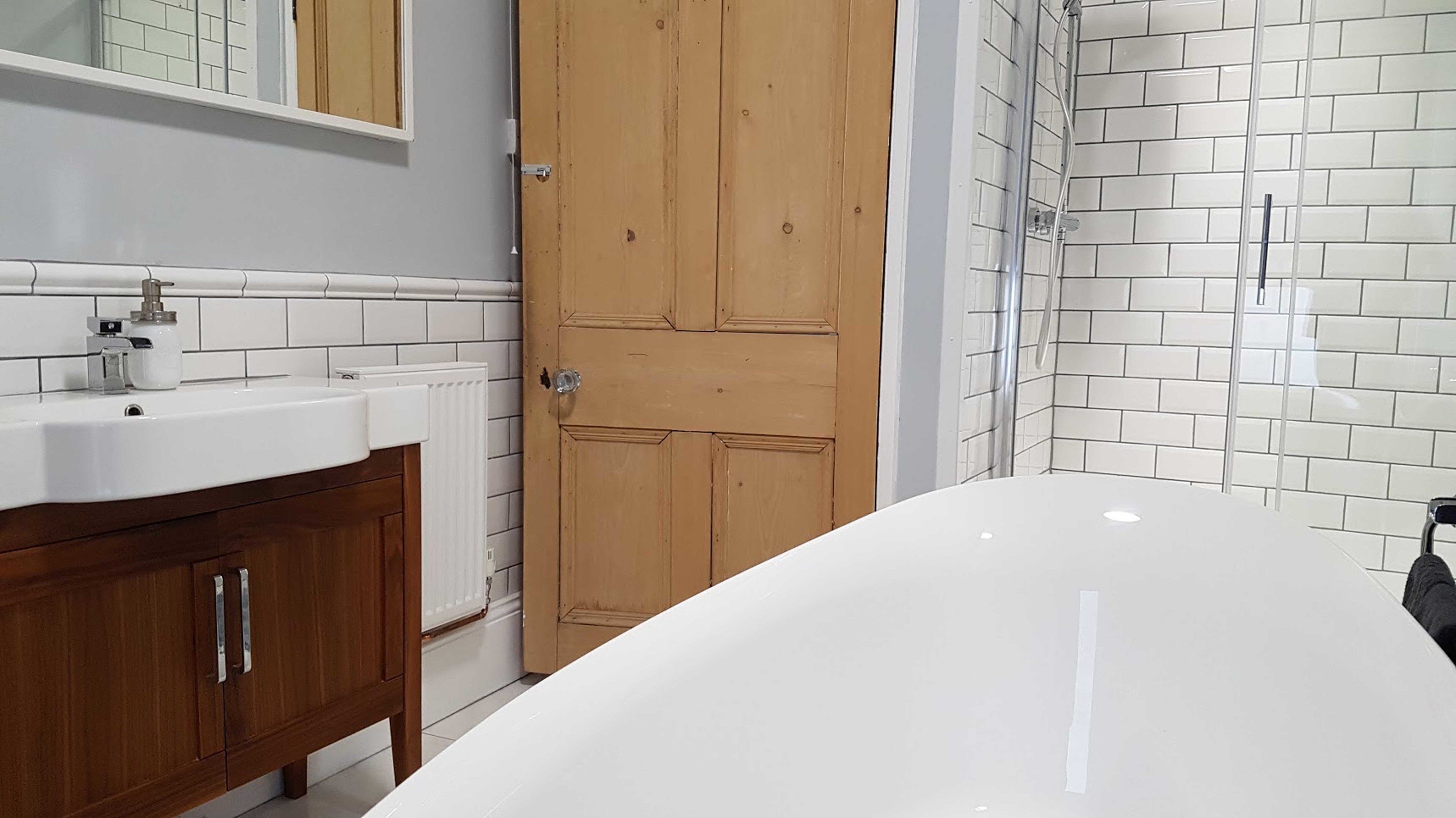 A bathroom with a white sink, wooden cabinet, and a shower area with white tiles.