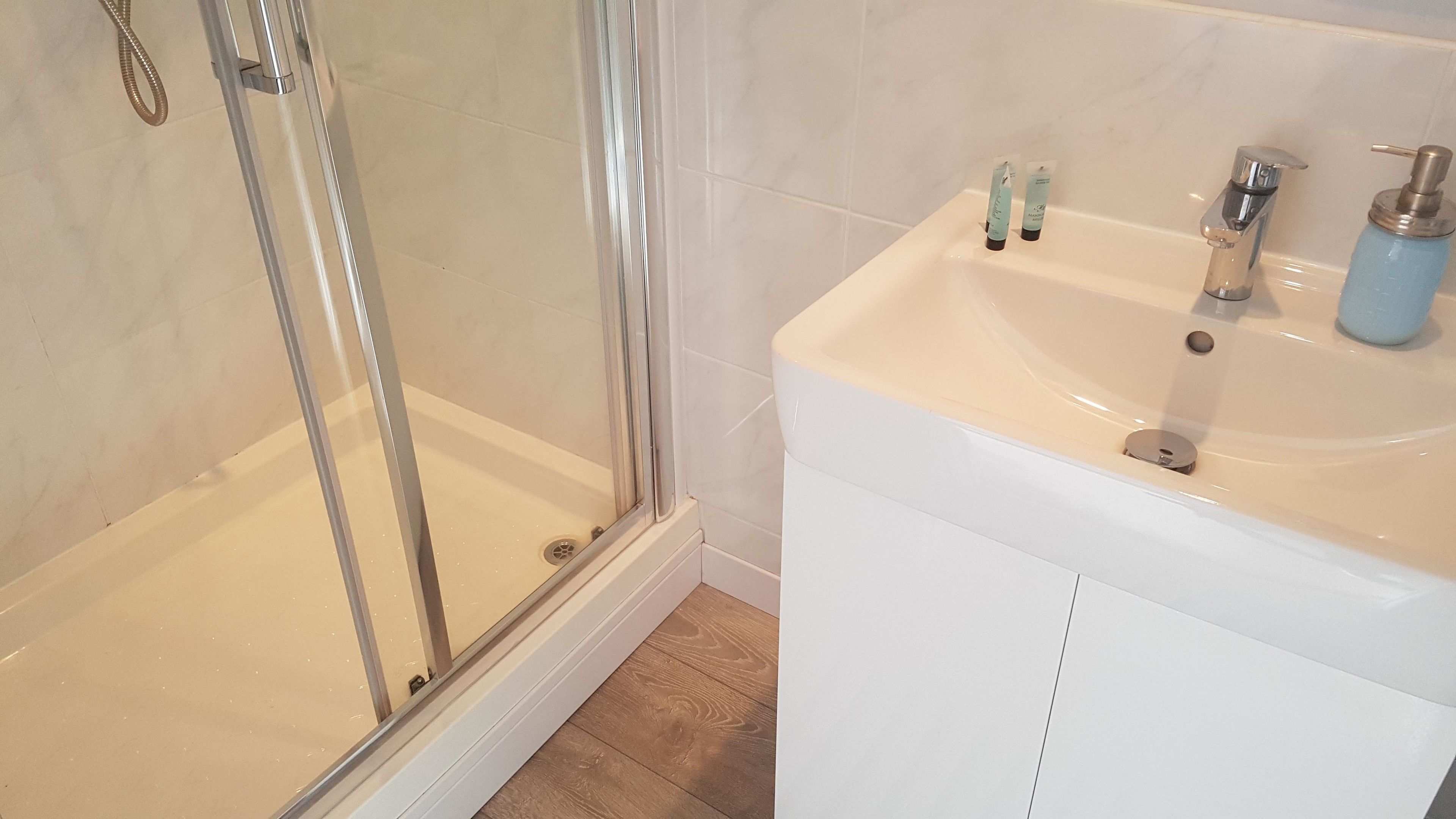 Un baño con ducha de vidrio y un lavabo blanco con dispensador de jabón.