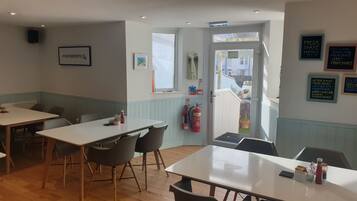 A dining area with tables and chairs, a fire extinguisher, and a window with a view of the outside.