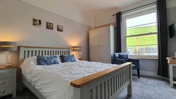 A bedroom with a bed, bedside tables, a wardrobe, a chair, a TV, and a window with a view of a field.