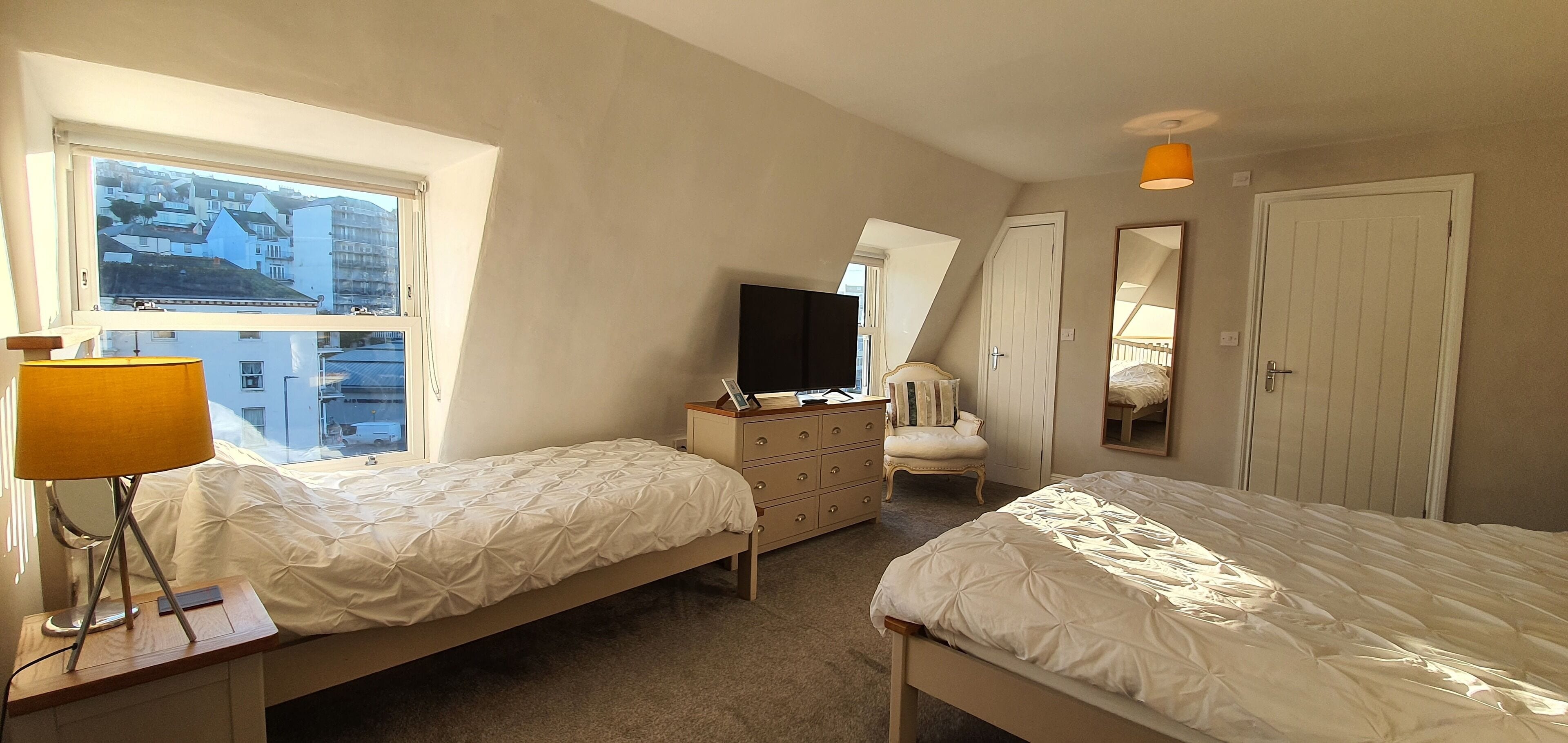 A bedroom with two beds, a dresser, a TV, and a window with a city view.