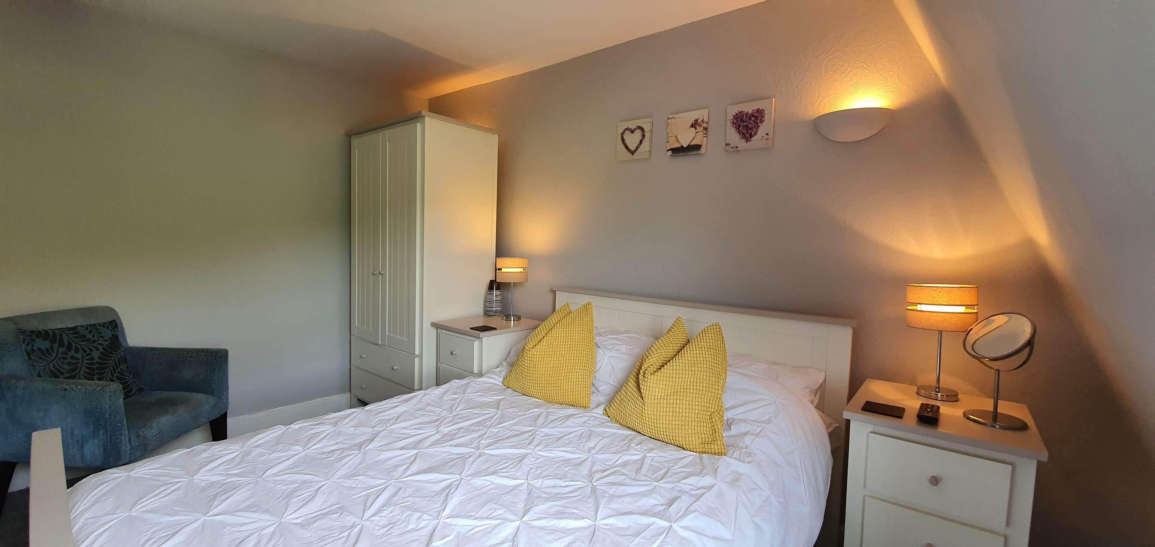 A bedroom with a bed, bedside tables, a chair, a wardrobe, and wall art.