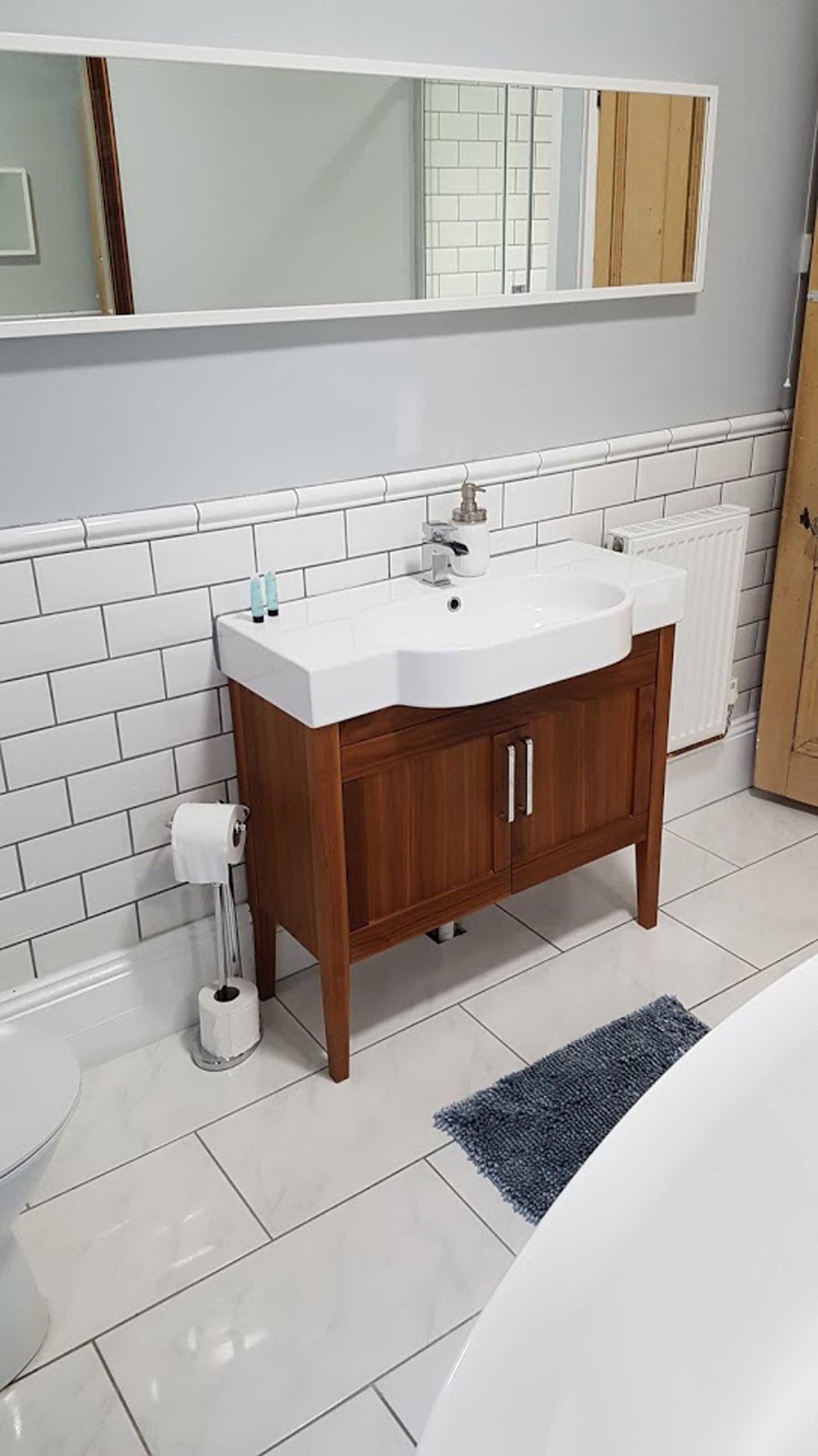 Ein Badezimmer mit einem weißen Waschbecken, einem Holzschrank und einer blauen Fußmatte.
