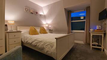 Un dormitorio con cama, mesitas de noche, televisión y ventana con vistas.