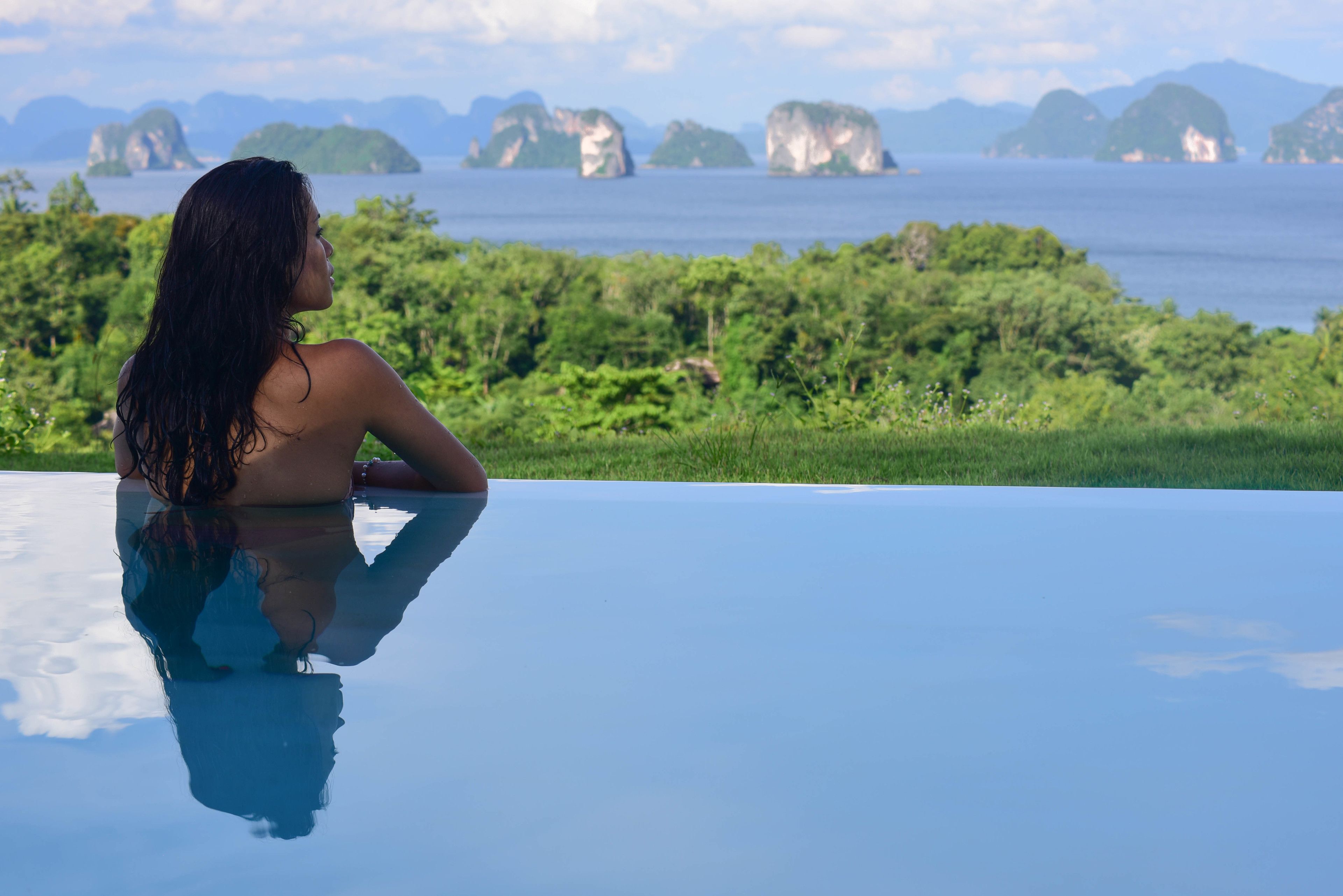A person relaxing by a reflective pool with a view of a tropical landscape and distant islands.
