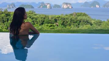 A person relaxing by a reflective pool with a view of a tropical landscape and distant islands.