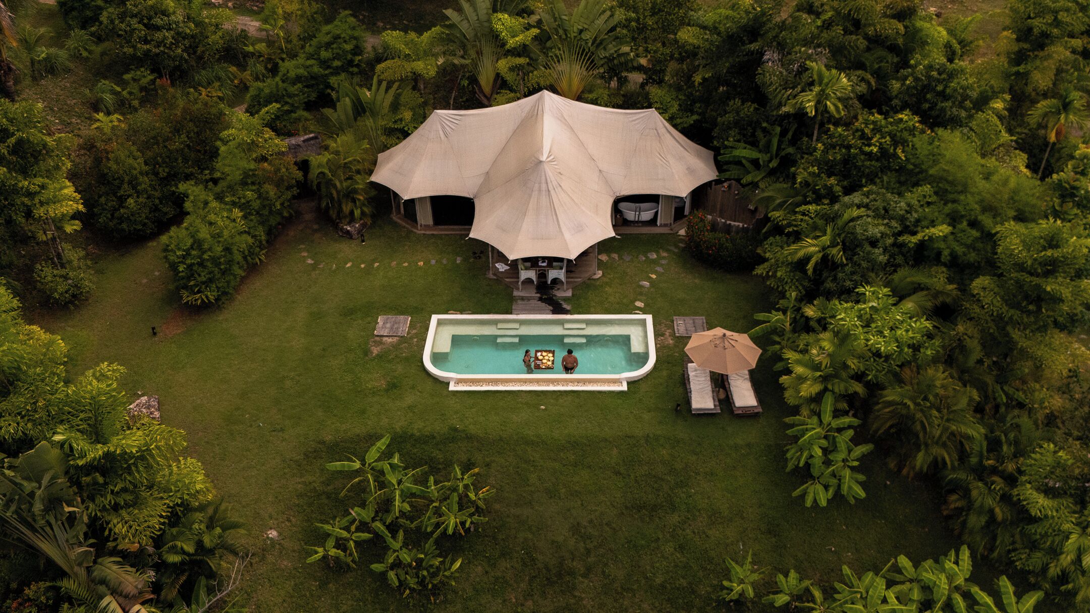 An aerial view of a resort with a swimming pool, lounge chairs, and a large umbrella structure.