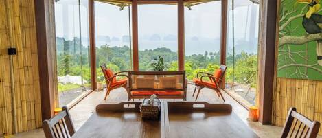 Comedor con mesa y sillas de madera, un banco acolchado y vistas a exuberante follaje y islas distantes.