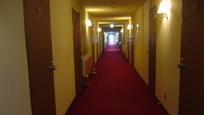 A hotel hallway with a red carpet, doors on both sides, and wall-mounted light fixtures. - Naeba Springs Hotel (Yuzawa)