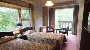 A room with two beds, a desk, a chair, and a balcony with a view of trees. - Naeba Springs Hotel (Yuzawa)