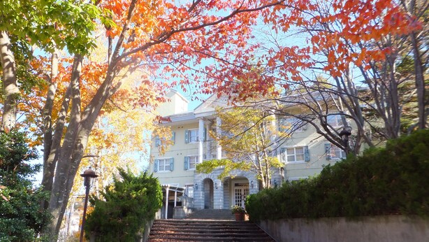 A building with a staircase leading up to a door, surrounded by trees with autumn leaves. - Naeba Springs Hotel (Yuzawa)
