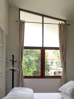 Una habitación con cama, perchero y ventana con cortinas.