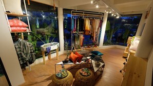 A cozy room with wooden flooring, a central table with cushions, and a clothing rack with various garments. - YATS Colony (Yogyakarta)