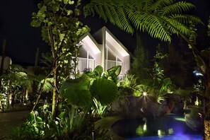 Una casa moderna con amplios ventanales y una piscina rodeada de exuberante vegetación.