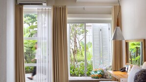 A hotel room with a large window, a bed, a bedside table, and a desk with a chair. - YATS Colony (Yogyakarta)