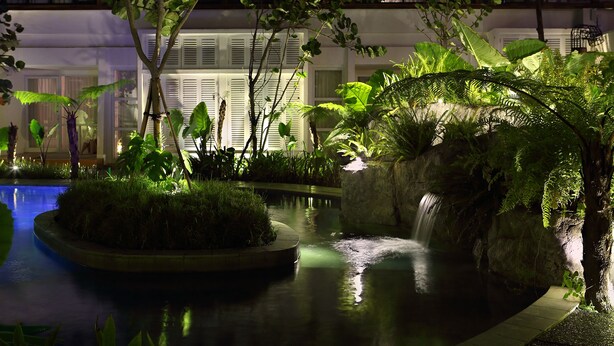A serene indoor garden with a small waterfall, lush greenery, and a pool. - YATS Colony (Yogyakarta)