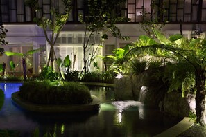 Un jardín interior tranquilo con una pequeña cascada, abundante vegetación y una piscina.