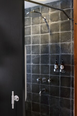 Un baño con ducha, un secamanos y dos botellas de jabón de manos en la pared.