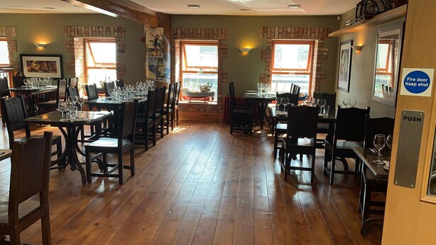 A restaurant with wooden floors and brick walls. Tables are set with wine glasses and plates. - Paul Arthur's Restaurant and Rooms - Kircubbin (Portaferry)