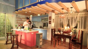 Una cocina con una isla central, taburetes de madera, una mesa de comedor con sillas y una araña.