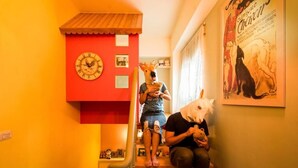 Una escalera con un reloj de pared rojo, una persona con máscara de reno y un cartel con un perro.