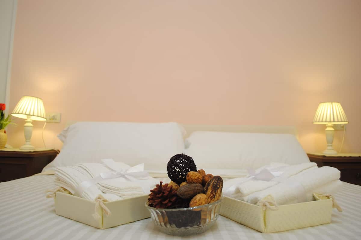 A neatly made bed with two bedside tables, each with a lamp, and a glass bowl containing nuts and a pine cone on the bed.