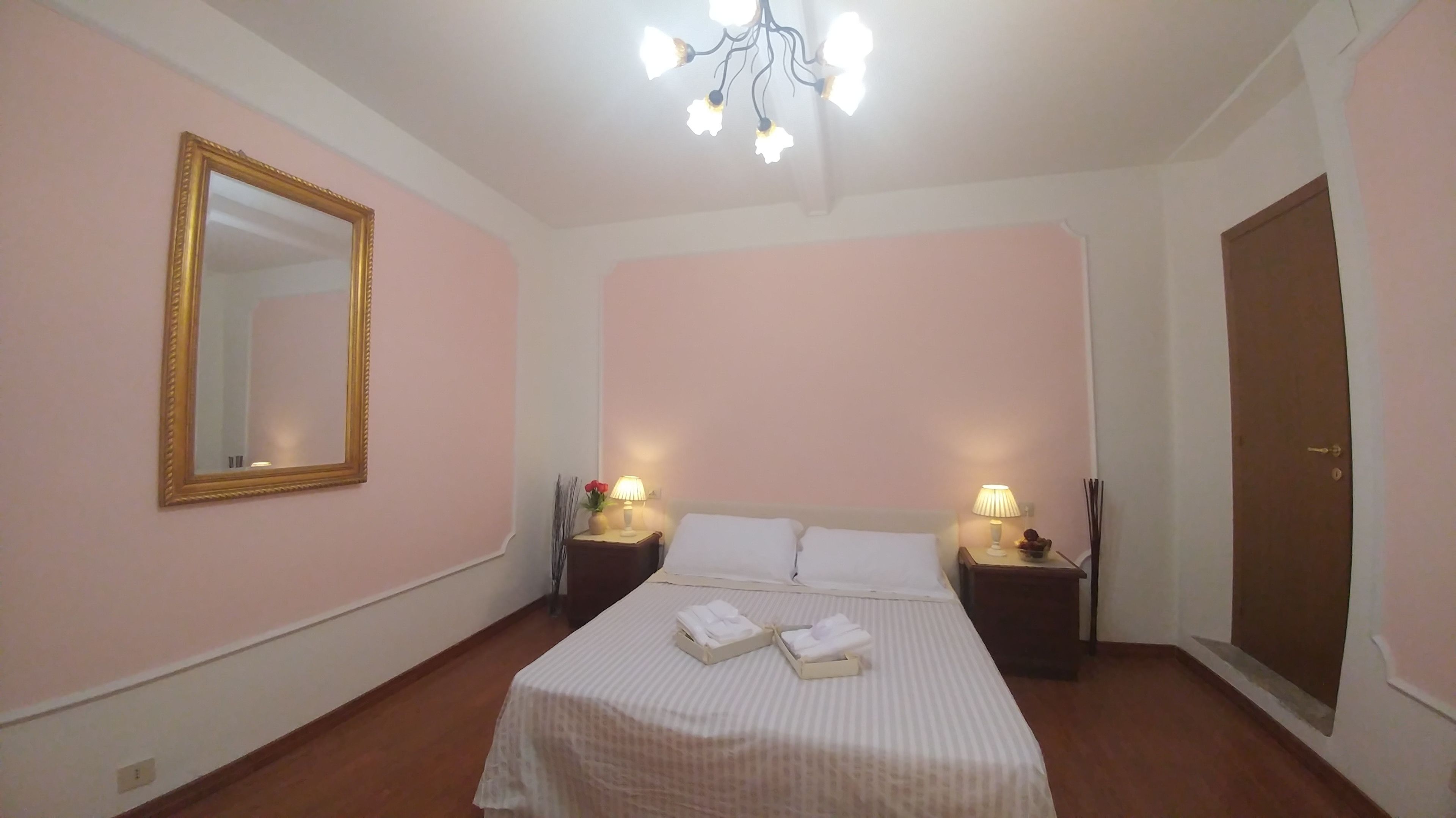 A hotel room with a bed, two bedside tables with lamps, a large mirror, and a wardrobe.