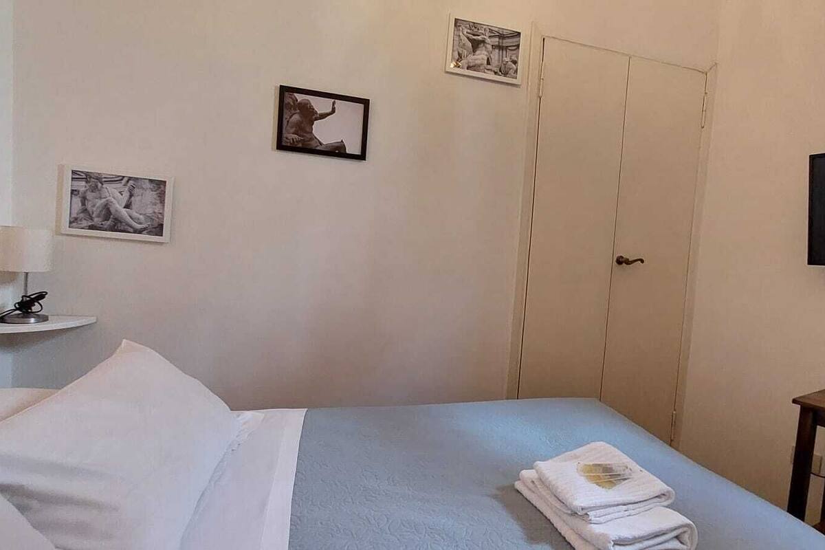 A hotel room with a bed, a TV mounted on the wall, and two framed pictures on the wall.