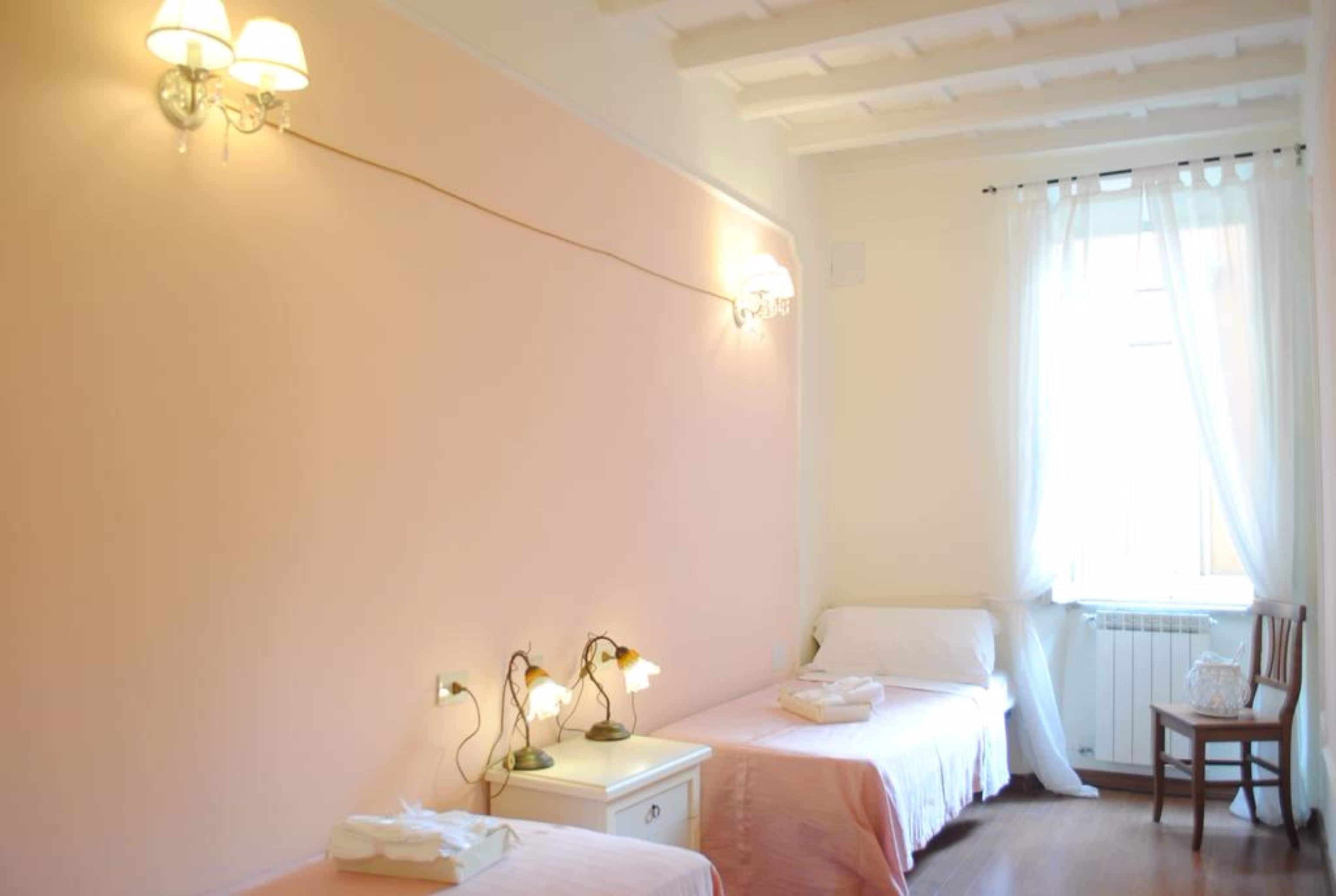 A bedroom with two beds, a nightstand, a chair, and a window with curtains.