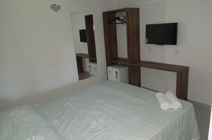 Une chambre à coucher avec un lit, une commode en bois, une télévision et un miroir.