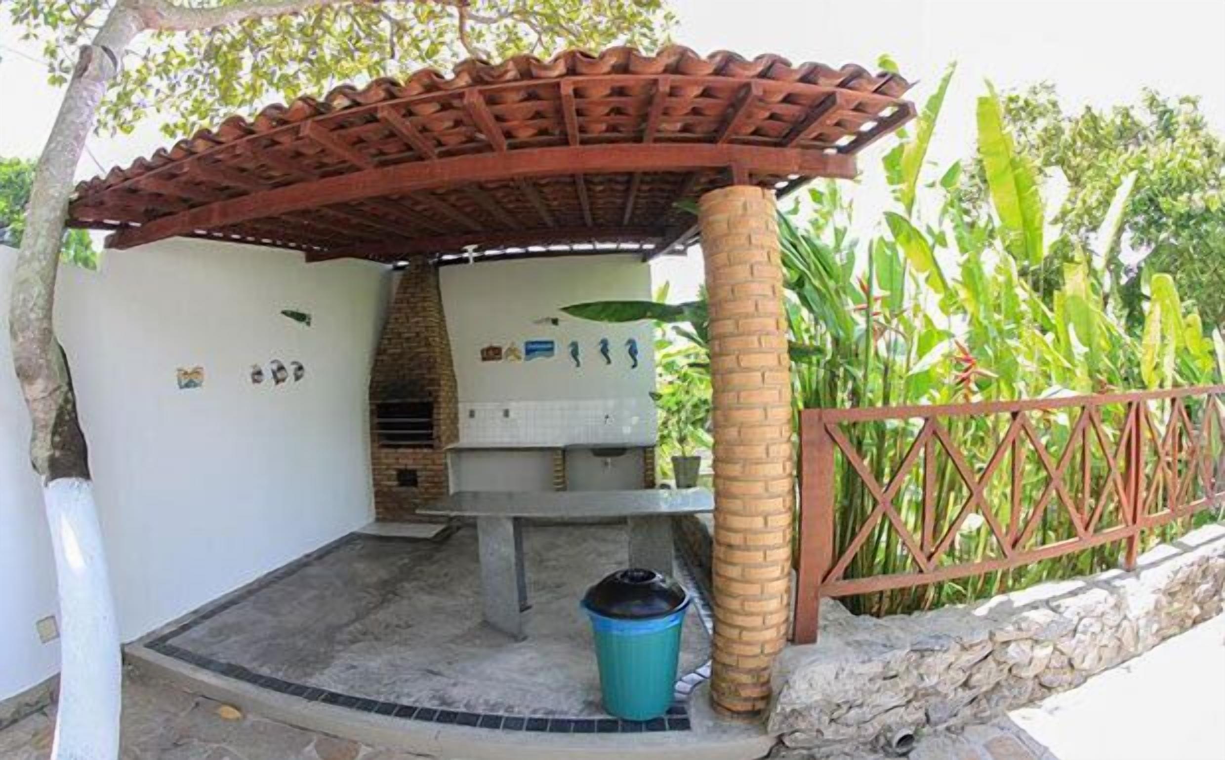 An outdoor barbecue area with a brick pillar, a grill, and a trash bin.
