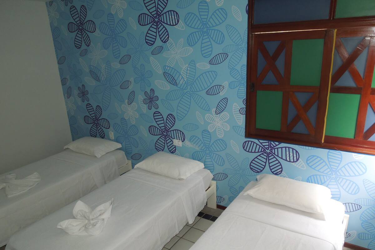 Una habitación con dos camas individuales, una pared azul con estampado y una ventana con marco de madera.