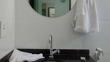 Une salle de bain avec un miroir rond, un lavabo, un porte-serviettes et un sèche-cheveux.