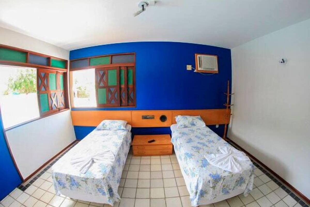 Una habitación con dos camas individuales, una ventana con vistas y un pequeño aire acondicionado en la pared.