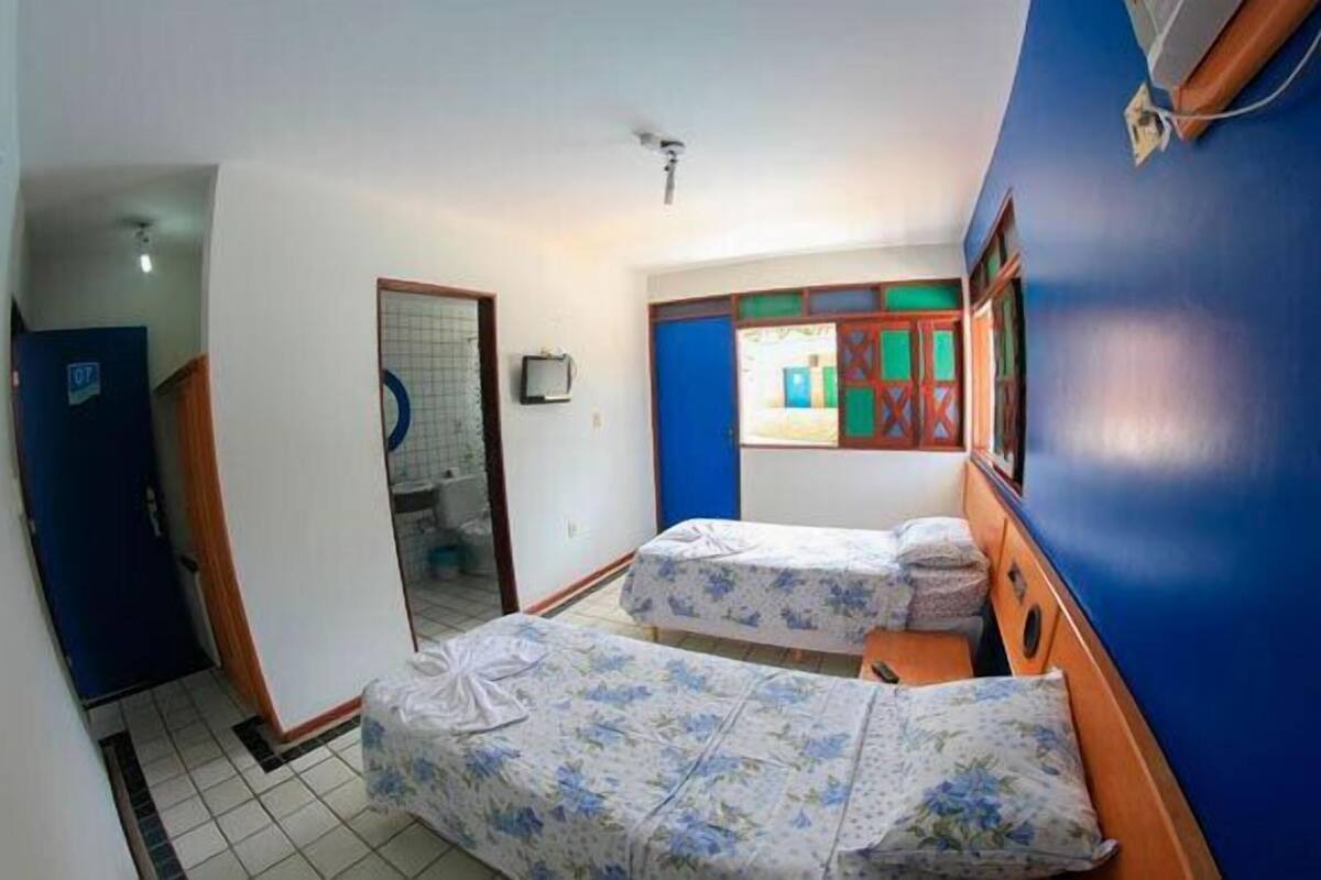 Una habitación con dos camas, un baño y un ventanal con persianas coloridas.