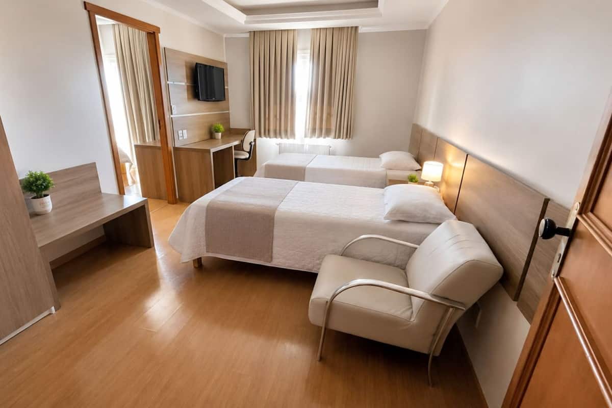 A hotel room with two beds, a desk, a chair, a TV, and a window with curtains.