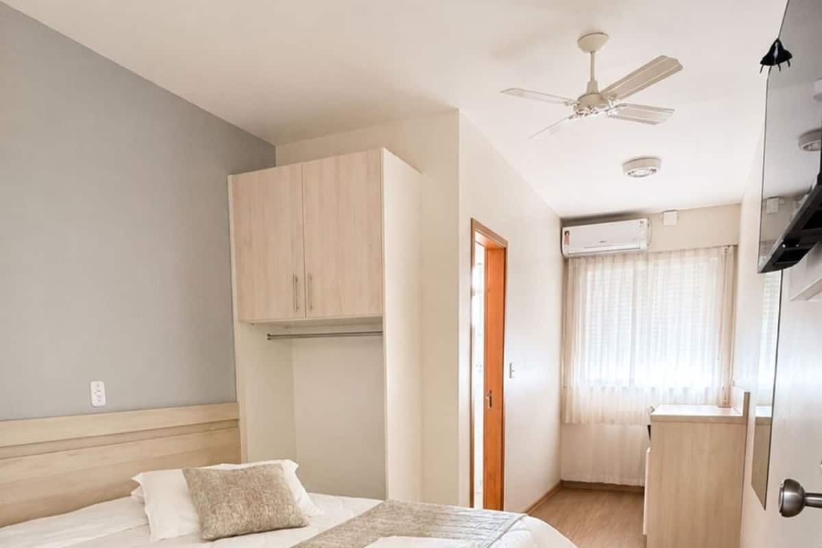 A bedroom with a bed, a ceiling fan, a window with curtains, and a small desk area.