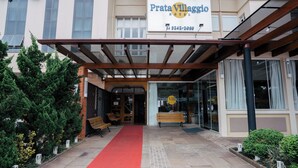 A hotel entrance with a red carpet, wooden benches, and a covered walkway. - Hotel Prata Villaggio (Nova Prata)