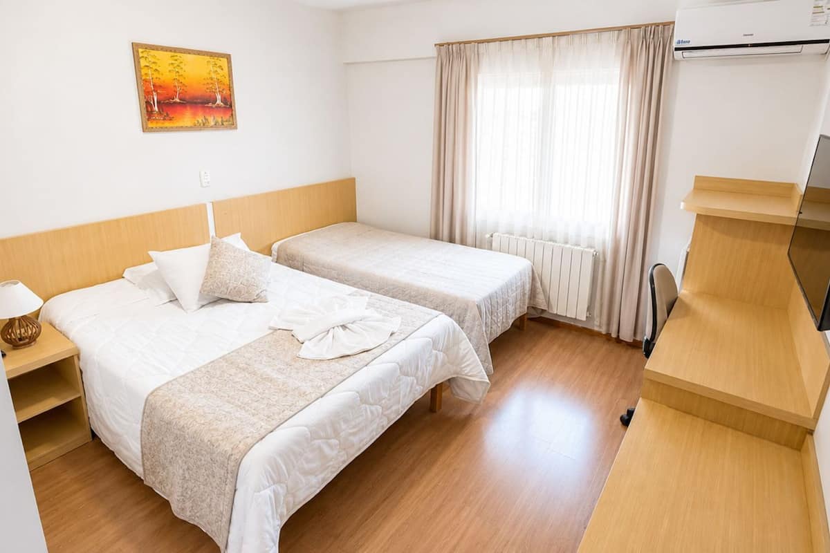 A hotel room with two beds, a painting, a TV, and a window with curtains.