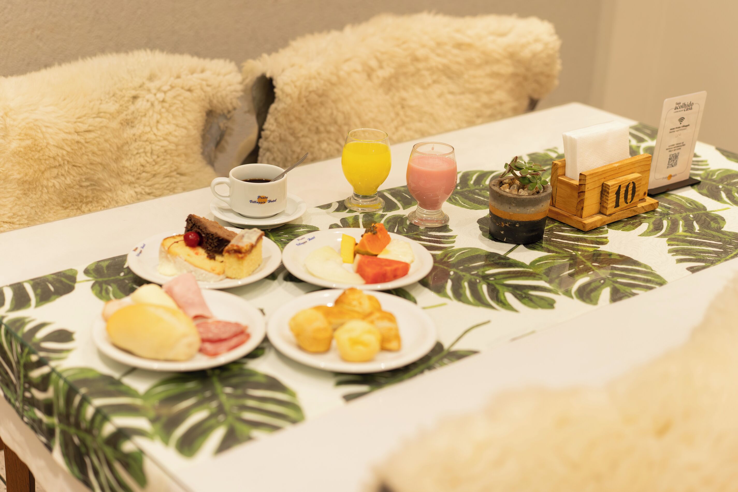 A breakfast table with plates of food, a coffee cup, juice glasses, a small plant, and a wooden sign with the number 10.