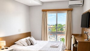 A hotel room with a bed, desk, TV, and an air conditioning unit. - Hotel Prata Villaggio (Nova Prata)