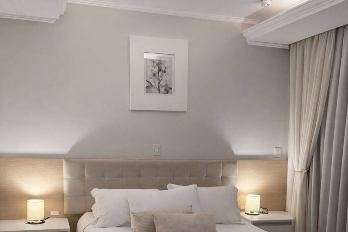 A bedroom with a large bed, two bedside tables with lamps, a ceiling light, and a framed picture on the wall.