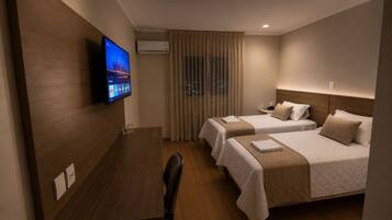 A hotel room with two beds, a desk, a TV, and an air conditioning unit.